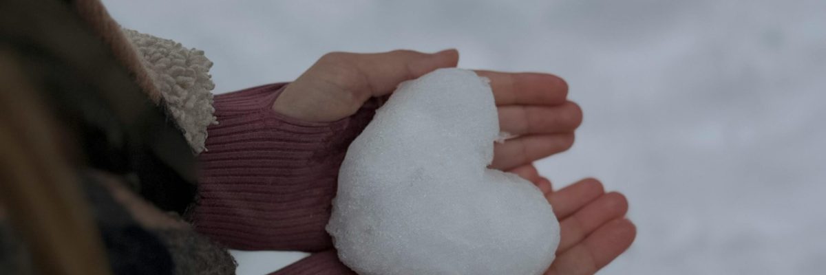 Hands holding a heart-shaped snowball on a winter day, symbolizing love.