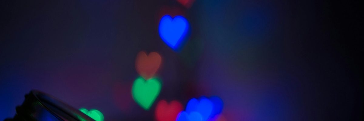Vibrant heart-shaped bokeh lights in blue, red, and green with a glass jar foreground.